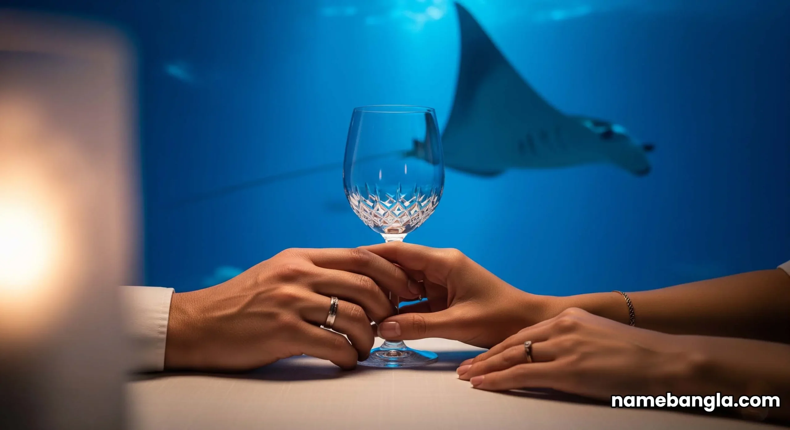 A couple dining at an intimate table, bathed in the deep blue light of a massive aquarium. A majestic manta ray is visible gliding past in the background.